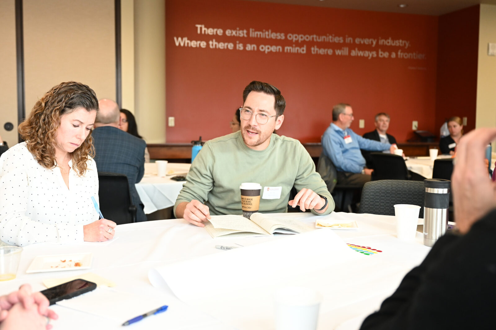 People sit at a table with pens and notebooks.