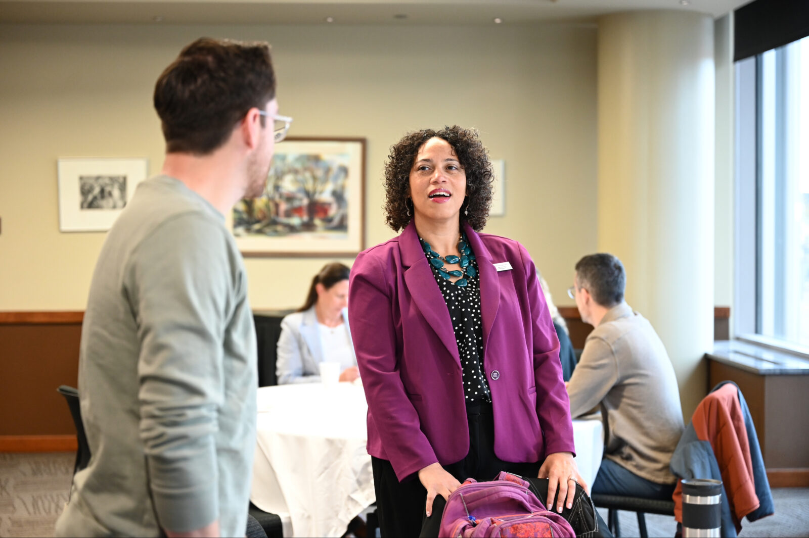 Two people speak to each other. One faces away from the camera, the other is turned torwards the camera.