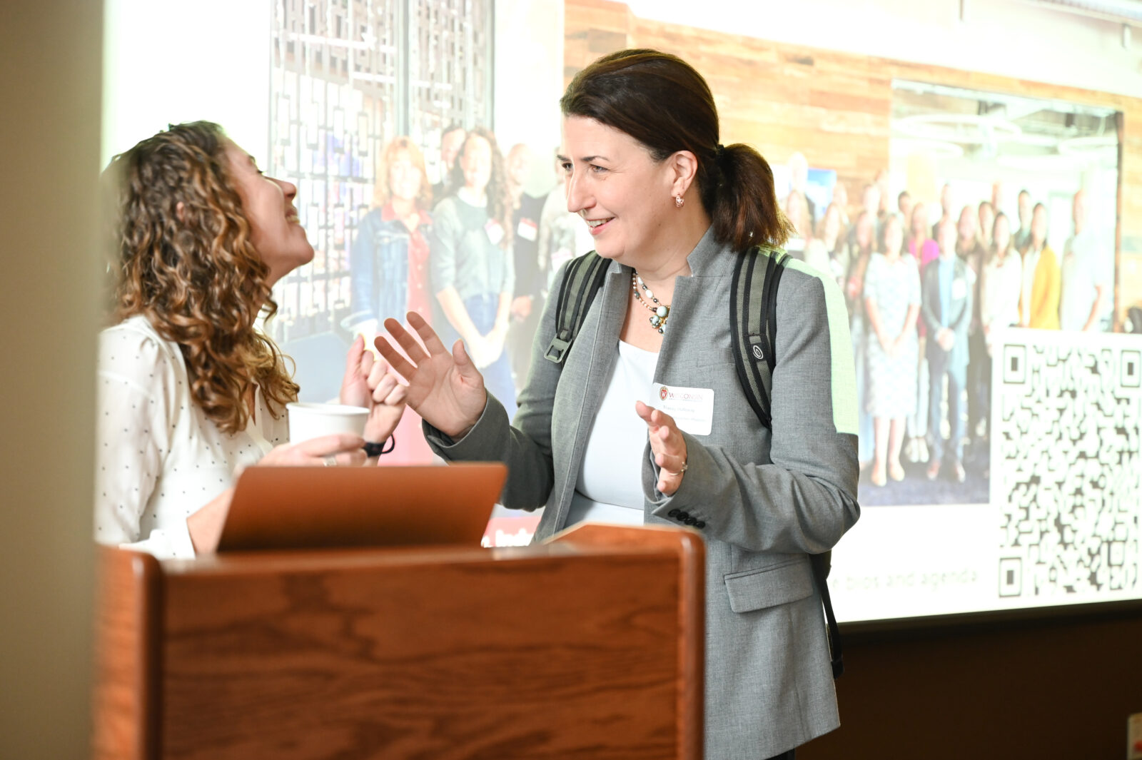 Two people talk to each other at a podium. One is smiling, the other is laughing. 
