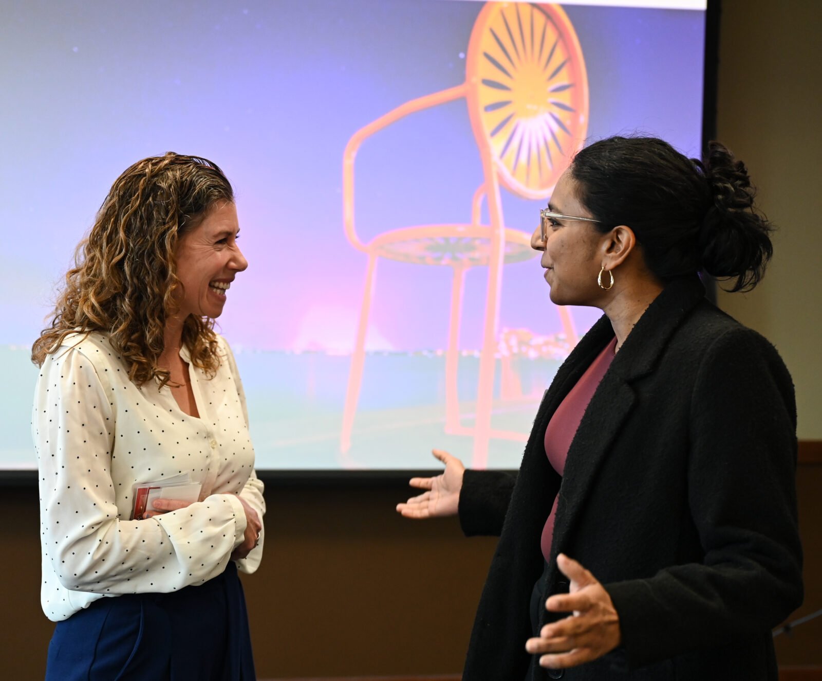 Two people talk in front of a Memorial Union Terrace Chair projected onto a presentation screen. 