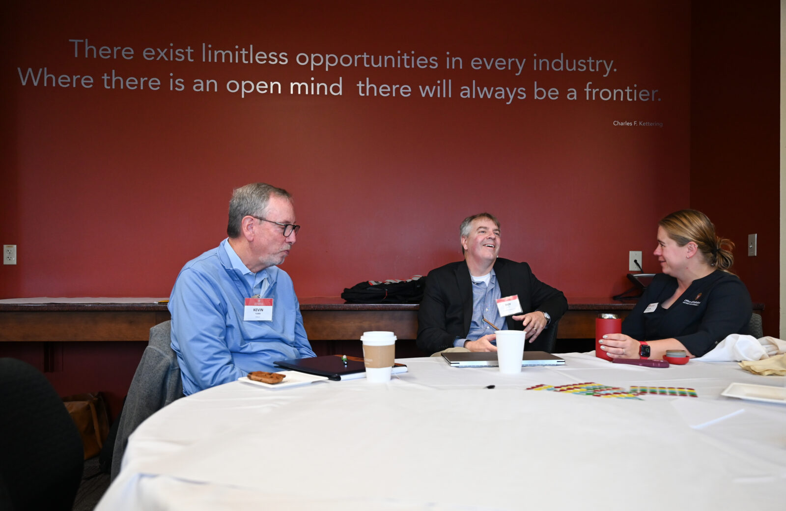 Three people are talking to each other, seated at a table. A quote in the background reads, "There exist limitless opportunities in every industry. Where there is an open mind, there will always be a frontier."