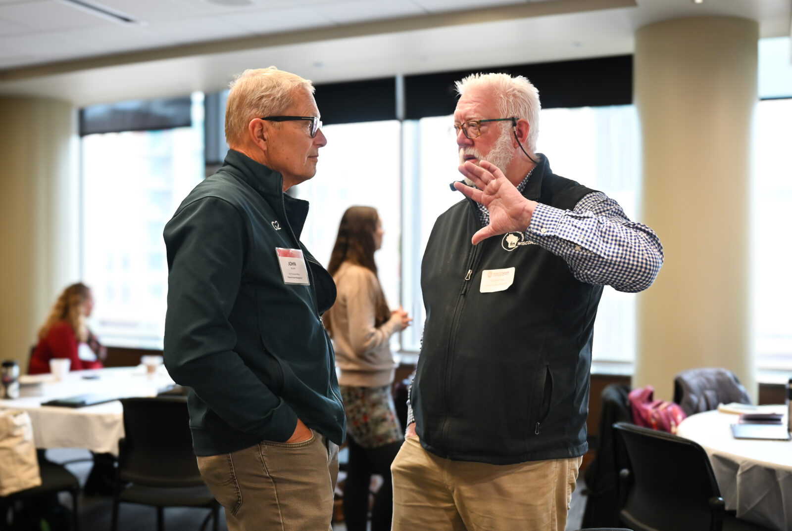Two individuals are facing each other and talking while standing.