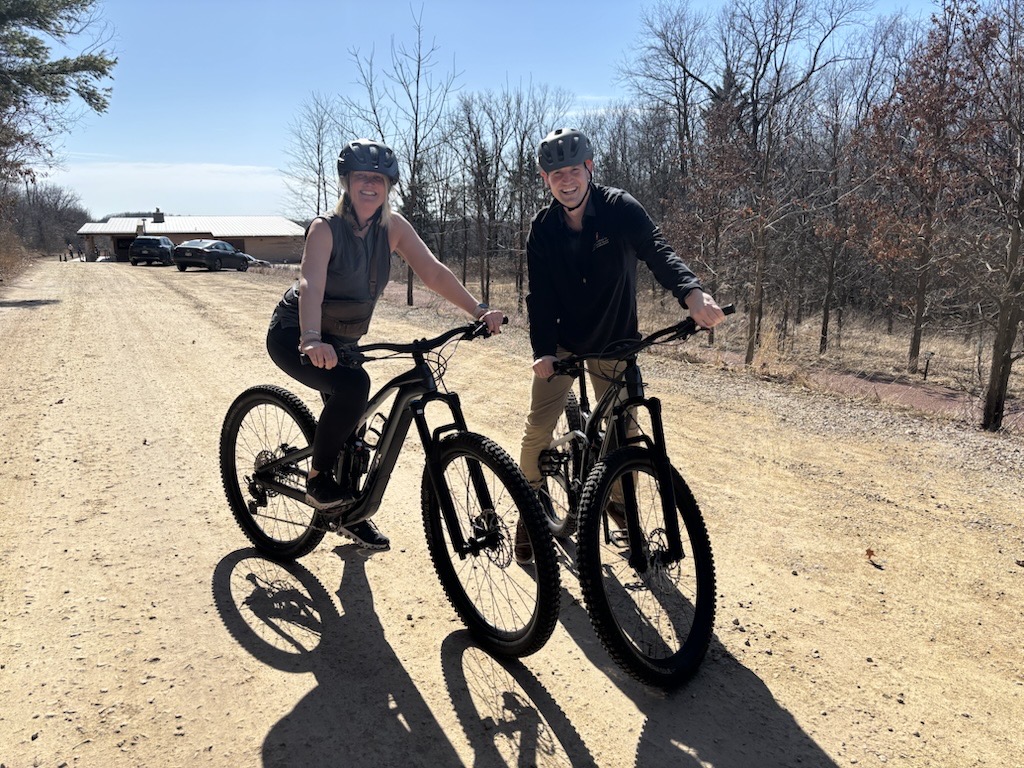 Two people wearing helmets are stopped on their bikes to pose for this photo.